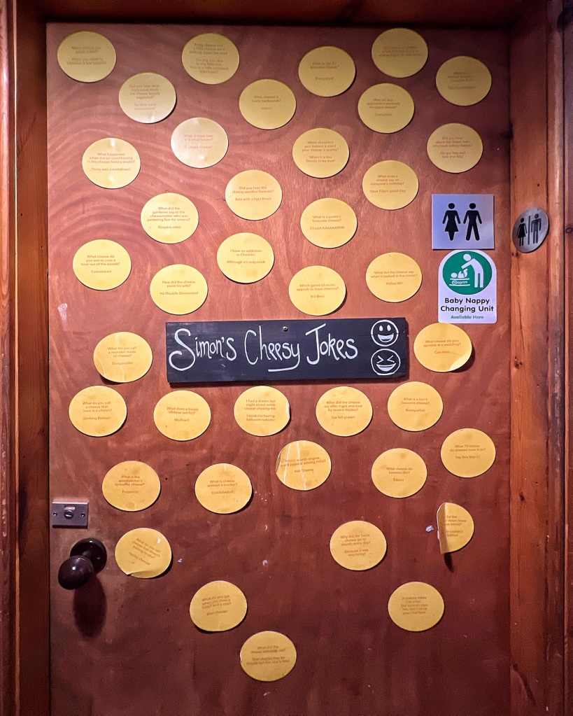 A door with a sign saying “Simon’s Cheesy Jokes” with laughing emojis on it, and lots of yellow circles with jokes printed on them all around it covering much of the door.